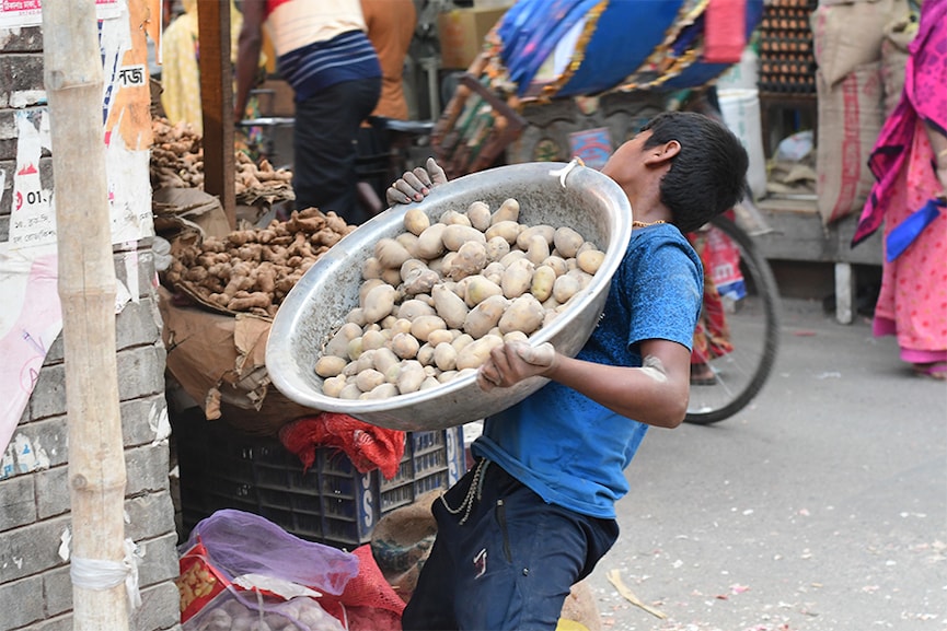 Alauddin, 10, whose family lost their home to flooding last year, works at a vegetable stand in Dhaka, Bangladesh, March 18, 2022. Image: Thomson Reuters Foundation/Mosabber Hossain