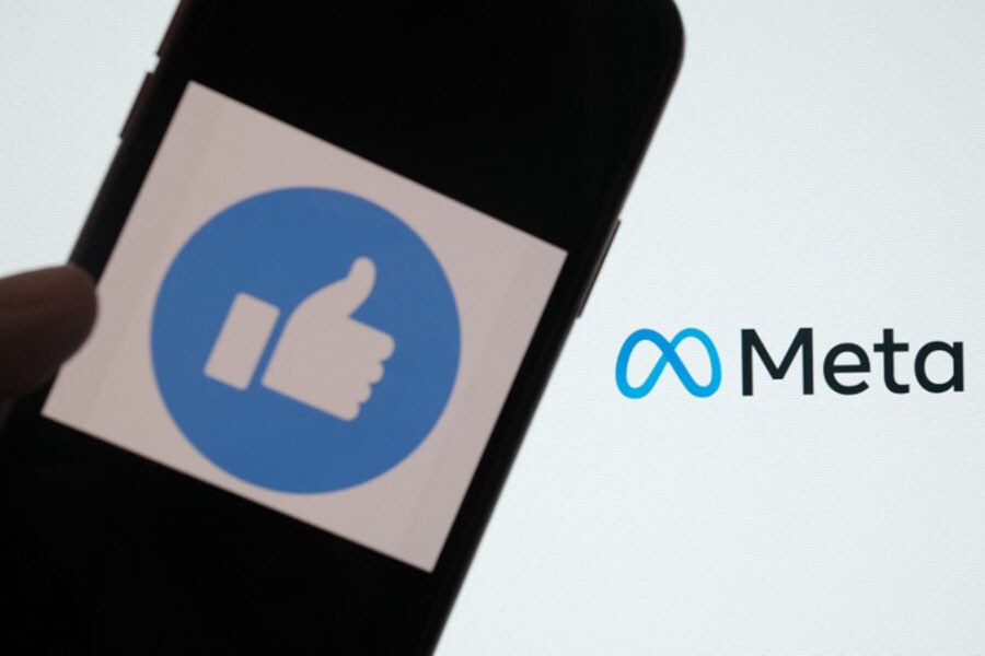 In this illustration photo taken in Los Angeles shows a person using Facebook on a smartphone in front of a computer screen showing the META logo. Facebook on October 20, 2022 added a method for people running groups to automatically sift out claims that have been debunked since being posted. Image: Chris DELMAS / AFP