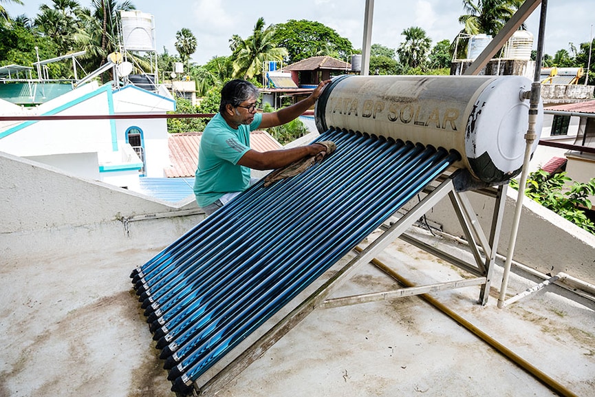 Martin Xavier, a resident of Naigaon, cleans his solar water heater, which he installed 14 years ago.