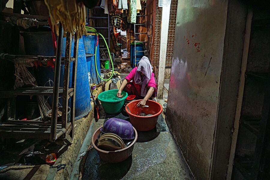 A woman washes dishes in the common area in Dharavi. Image: Mexy Xavier