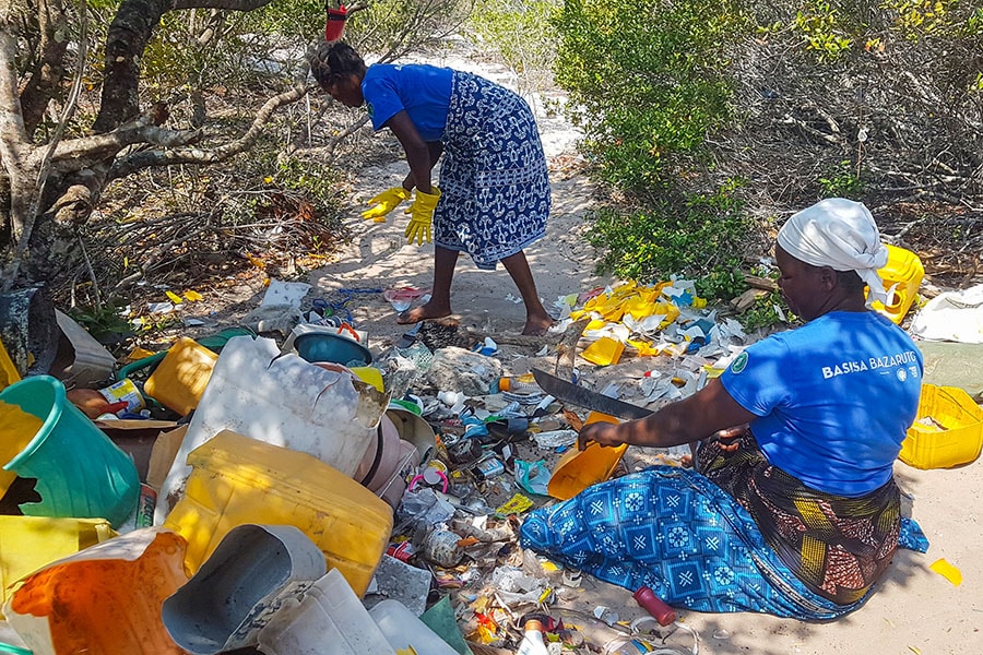 Rebecca Banze and Judite Huo at work: 39-year-old (R) Rebecca Banze is chopping a discarded plastic container into smaller pieces using a machete. Image: Khursheed Dinshaw