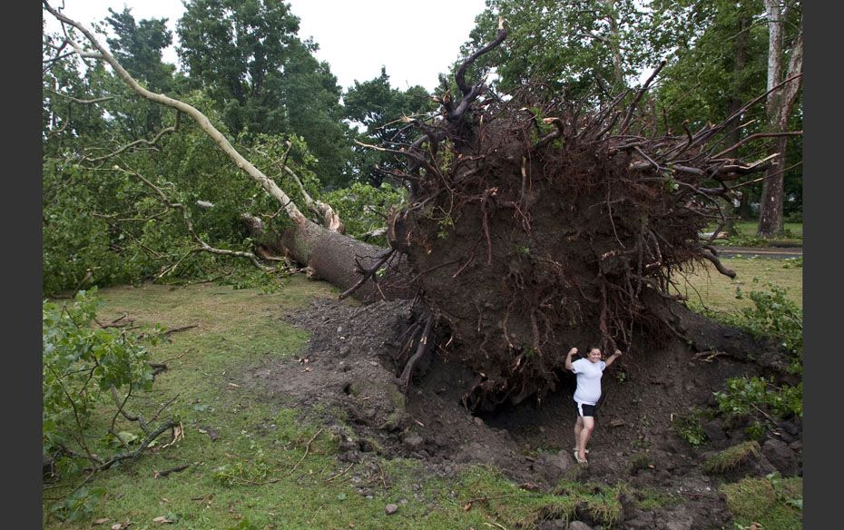 Jessica Stansfield poses for a photo below an enormous uprooted tree in  Elmira, New York, after the