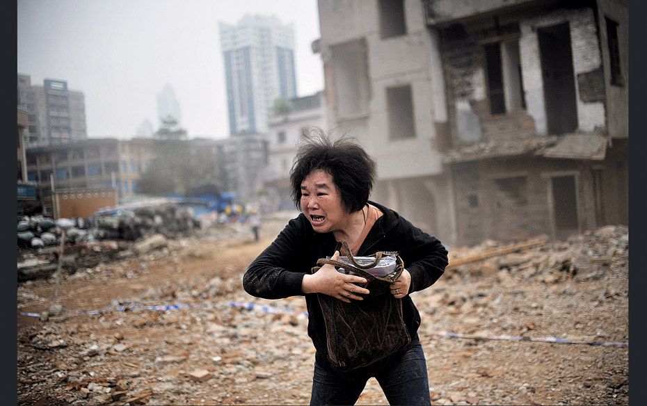 A woman reacts as she sees a part of her house being demolished as part of China’s relentless 