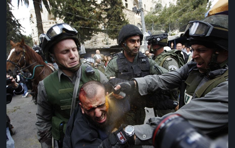 Israeli border police officers use pepper spray as they detain an injured Palestinian protester duri