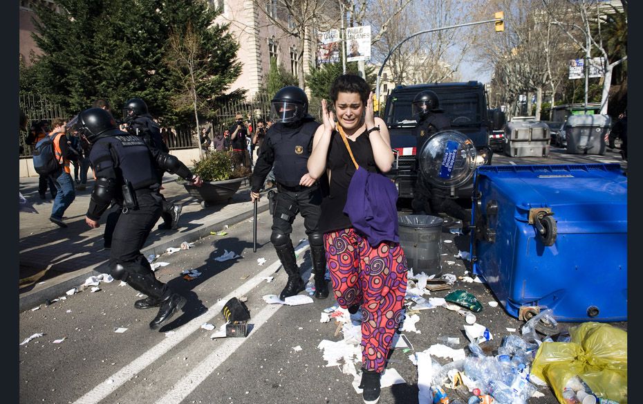 A student runs for cover as riot police try to quash a demonstration in Barcelona, Spain. Student as