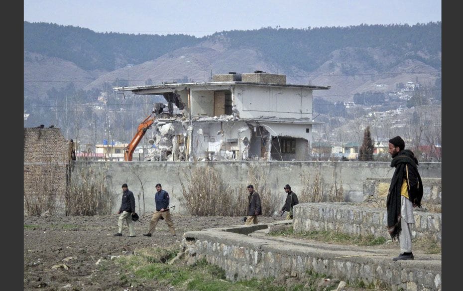 Policemen walk past while demolition work is carried out on the building where al Qaeda leader Osama