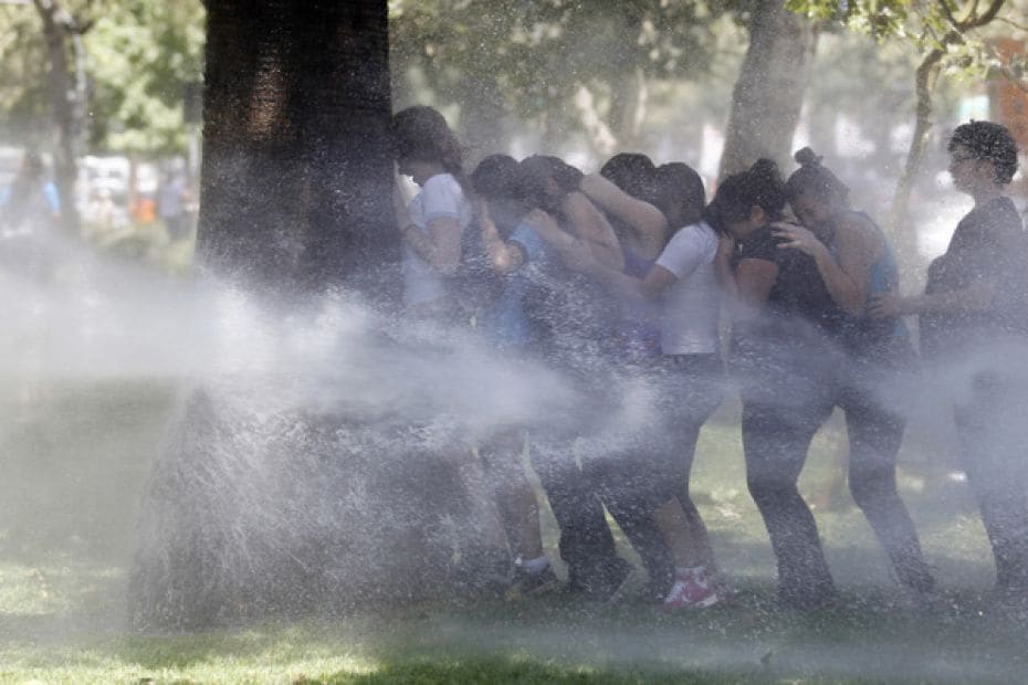 Students take cover behind a tree from water sprayed by riot policemen during a protest against the 