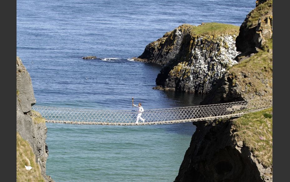 Charity fundraiser Denis Broderick carries the Olympic torch across Carrick-a-Rede rope bridge near 