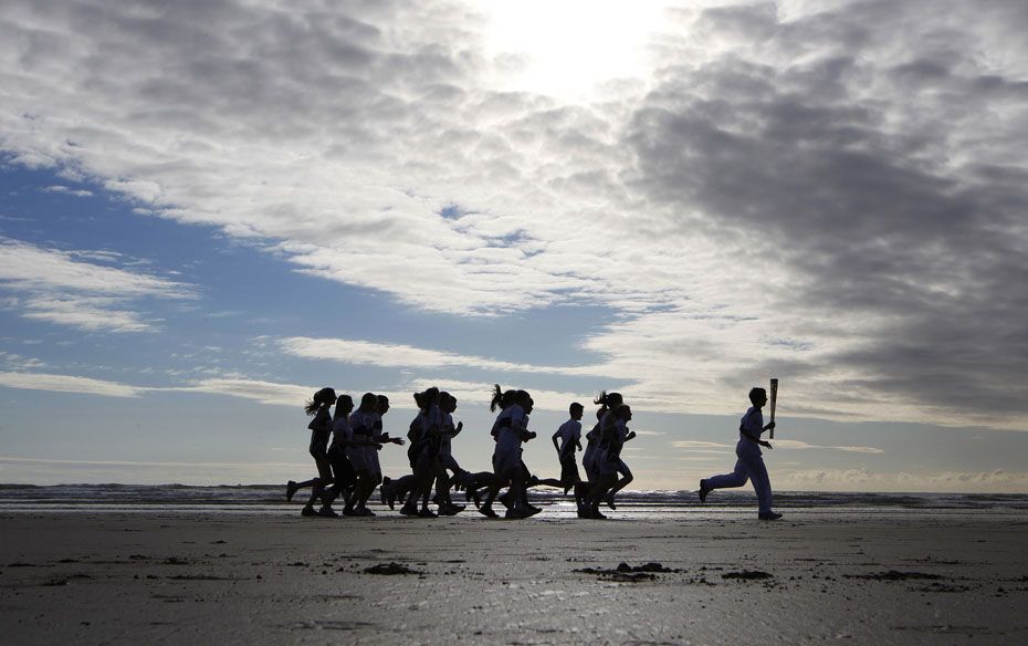 Torch bearer Joeseph Forrester is followed by school children as he runs with the London 2012 Olympi