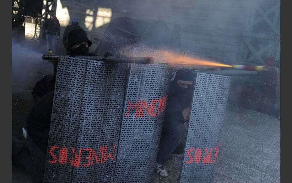 A coal miner hides behind shields, which read "miners", as he fires a home-made rocket dur