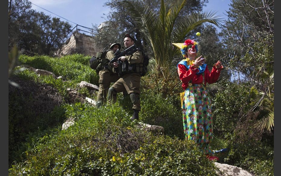 Israeli soldiers (l) stand guard as a man dressed as a clown juggles during a parade for the Jewish 