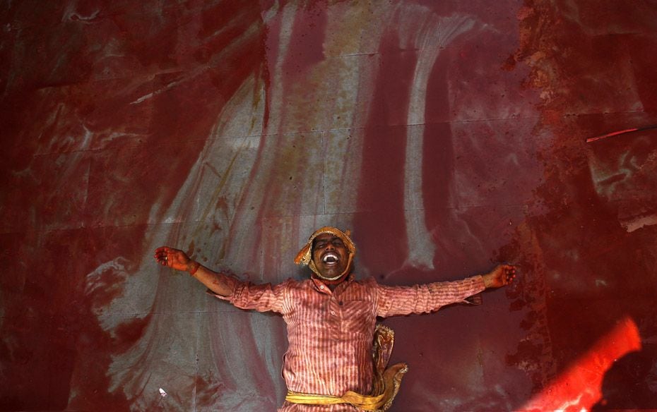 A man daubed in coloured powder lies on the ground as he celebrates "Lathmar Holi" at Nand