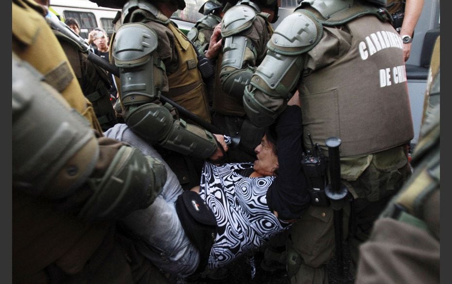 A protester in Santiago, Chile, is detained by riot police while protesting for fuel subsidies and s