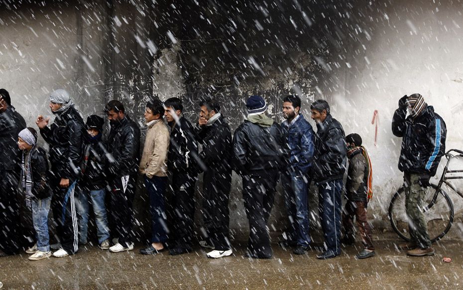 Men wait in front of a bakery to buy bread during winter in Al Qusayr, Syria                        