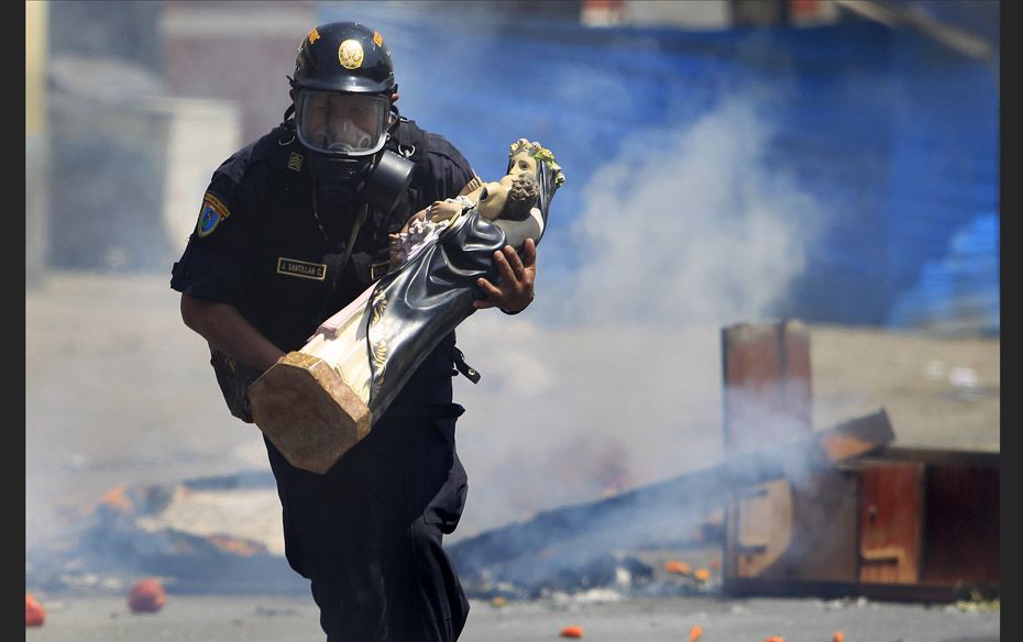 A policeman removes a statue of Saint Rose from a barricade during clashes between workers and resid