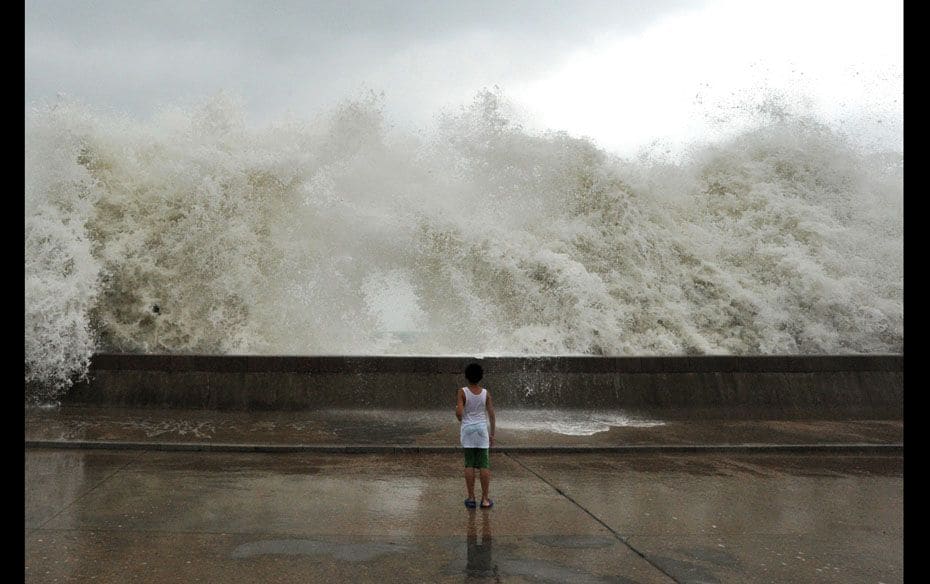 A child watches as high waves caused by typhoon Bolaven crash over the side of a road barrier in Qin