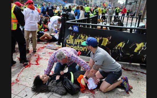 Bystanders help an injured woman at the scene of the first explosion on Boylston Street near the fin