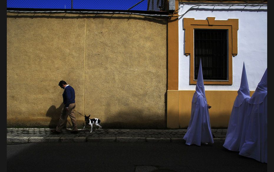 Penitents pass a man with a dog as they walk to a church before taking part in the procession of &ls