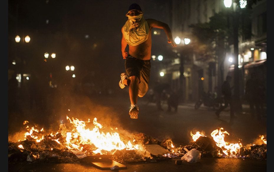 A demonstrator jumps over trash set afire during protests against poor public services, police viole