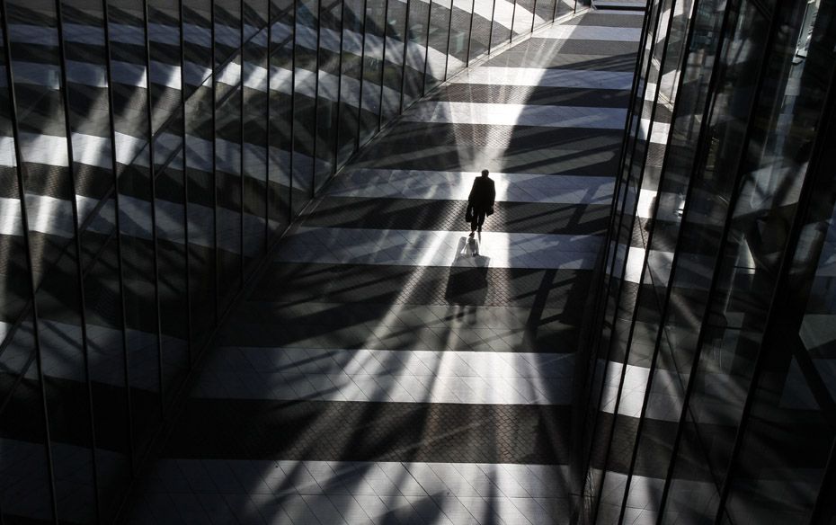 A man walks between glass facades of the Bonn Post Tower, the headquarters of German postal and logi