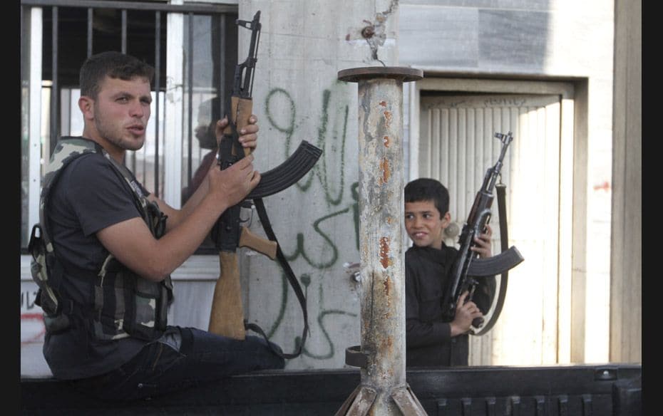 A Free Syrian Army fighter and a boy hold up weapons on a street at the Syrian town of Tel Abyad, ne