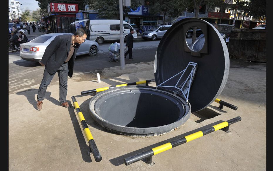 A man looks into a newly-built giant trash can, partially buried underground, next to a street in Ta