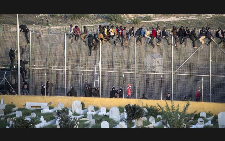 African migrants sit atop a border fence as Spanish Civil Guard officers try to turn them back durin