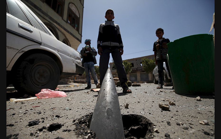 Boys stand in front of an artillery shell partially buried in the ground a day after the street was 