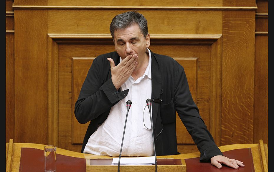 Greek Finance Minister Euclid Tsakalotos reacts as deputies disrupt his speech during a night parlia