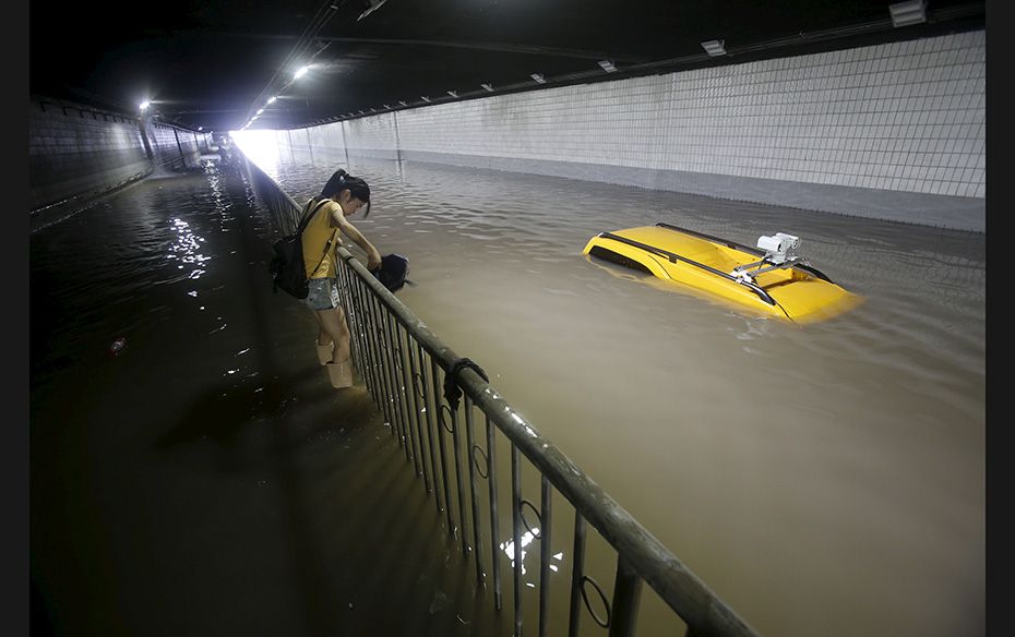 A woman walks past a stranded car as she tries to cross a flooded tunnel in Wuhan, Hubei province, C