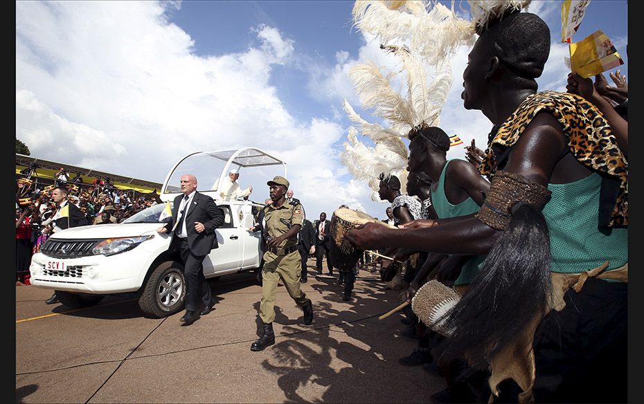 Performers wearing traditional tribal clothing greet Pope Francis as he arrives at the Kololo air st