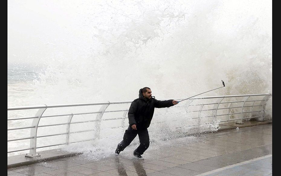 A man takes a selfie by a crashing wave on Beirut's Corniche, a seaside promenade, as high winds