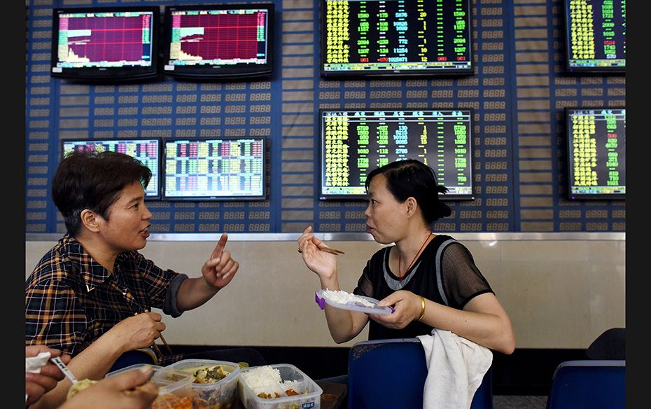 Investors have a meal in front of screens showing stock information, at a brokerage house in Hefei, 