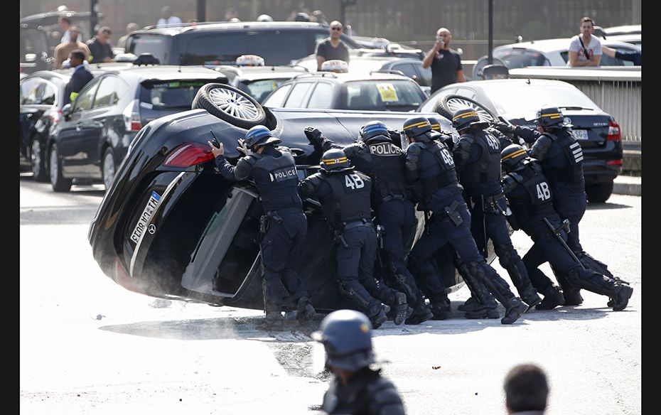 French riot police push an overturned car as striking taxi drivers demonstrate at the Porte Maillot 