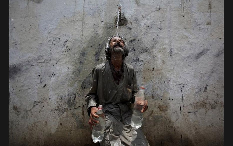 A man cools off from a public tap after filling bottles in Karachi on June 23. Intense heat waves in