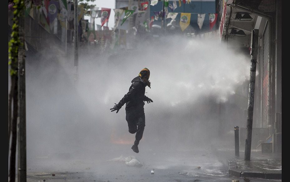 A masked protester runs away from a water cannon’s jet during clashes with police in Okmeydan