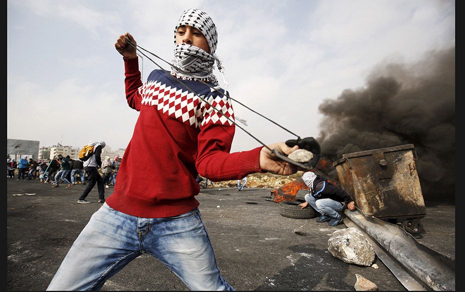 A Palestinian protester uses a sling to throw stones at Israeli troops during clashes near the Jewis