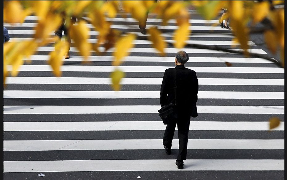 A businessman crosses a road under autumn leaves at Tokyo's business district in Japan on Novemb