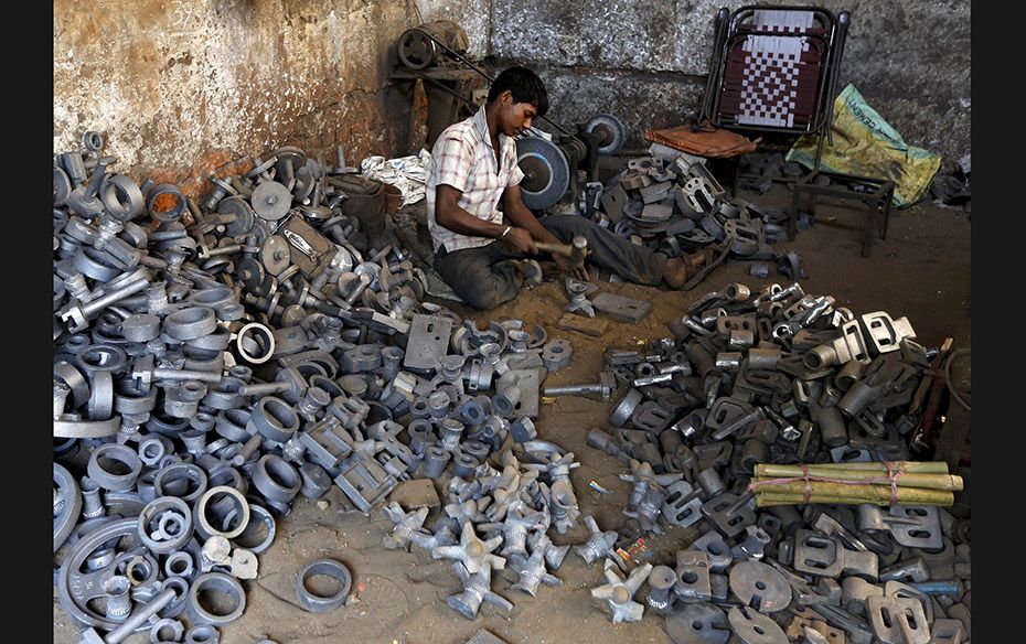 A worker separates casting joints of gearboxes inside a small-scale automobile manufacturing unit in