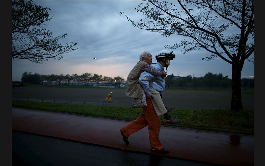 An elderly woman is carried by an ambulance worker after being rescued by a helicopter from an area 