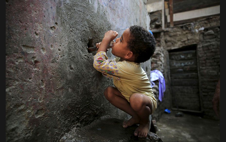 Five-year-old Karkar tries to drink water from a faucet near his home in the Eshash el-Sudan slum in