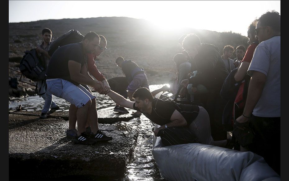 A Syrian refugee is helped out of a dinghy that deflated due to the rocks on the shore, on the isola