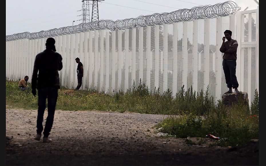 Migrants telephone near a fence topped with barbed wire near the makeshift camp called ‘The Ne