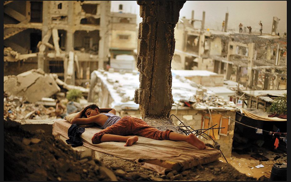 A Palestinian boy sleeps on a mattress inside the remains of his family’s house during a deadl