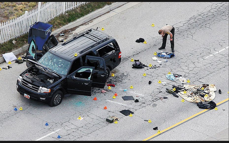 A law enforcement officer looks at evidence near the remains of an SUV following a mass shooting at 