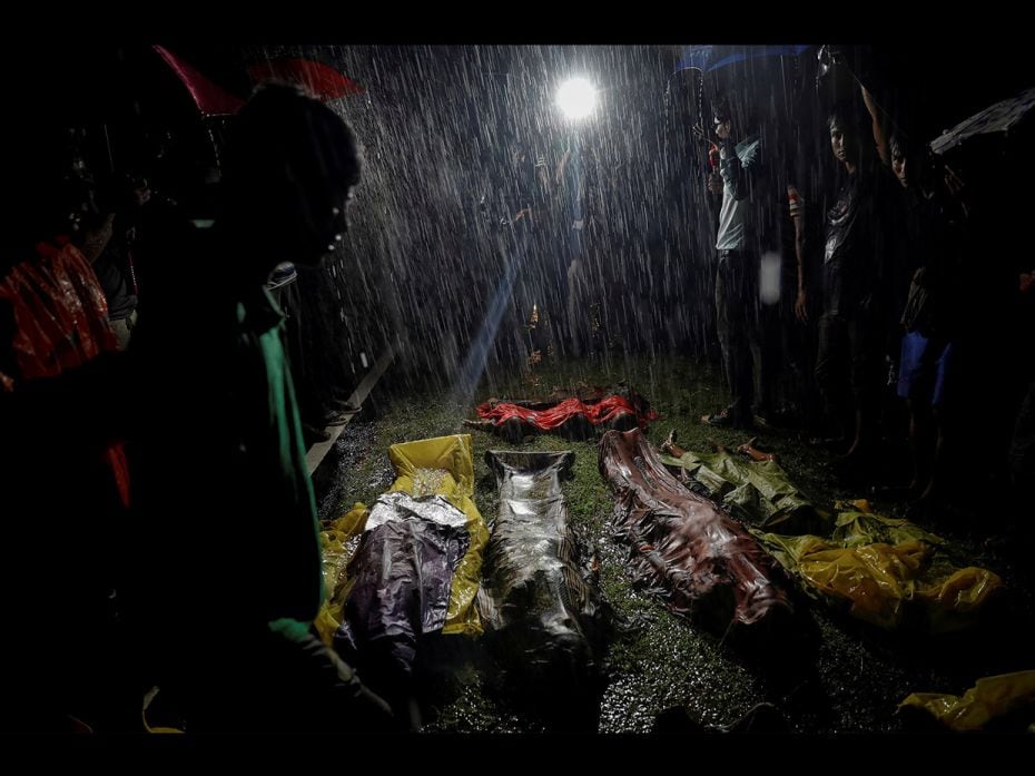 People gather under heavy rain around bodies of Rohingya refugees after the boat they were using to 