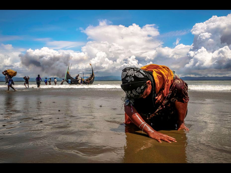 An exhausted Rohingya refugee woman touches the shore after crossing the Bangladesh-Myanmar border b