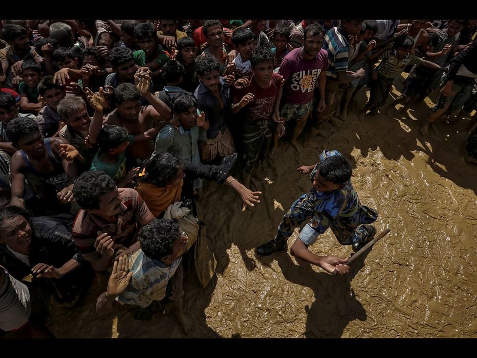 A security officer attempts to control Rohingya refugees waiting to receive aid in Cox's Bazar, 