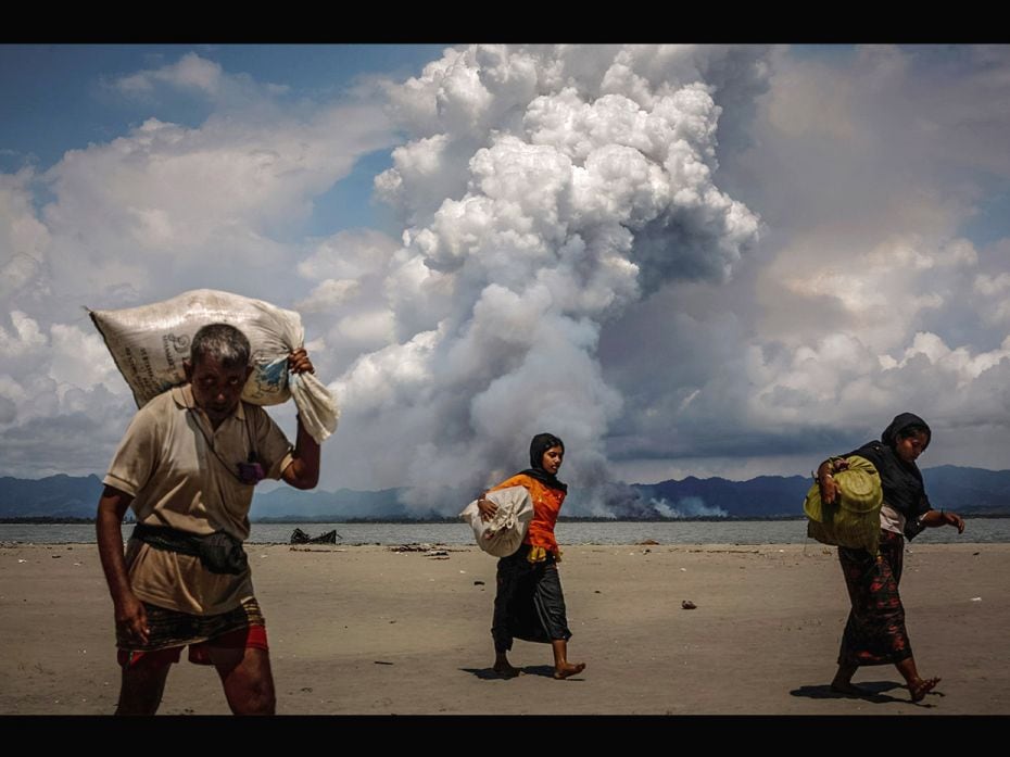 Smoke is seen on the Myanmar border as Rohingya refugees walk on the shore after crossing the Bangla