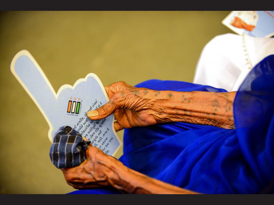 An image of an Indian centenary voter holding the leaflet abut voting, written in Gujarati. People h